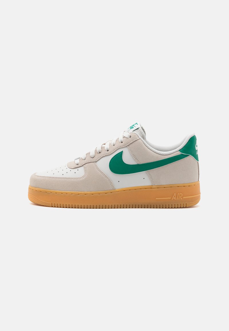 Tênis Nike Air Force 1 com parte superior em couro branco, detalhes em camurça cinza claro, swoosh verde e sola de borracha natural. Apresenta um design de amarração.
