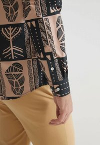 Chemise à manches longues en tissu rose et noir, ornée de motifs géométriques et de pois. Détails des poignets boutonnés visibles au poignet.