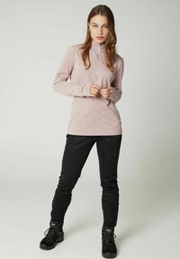 Helles rosa Langarm-Zip-Up-Oberteil aus strukturiertem Stoff mit Daumenlöchern, kombiniert mit schwarzen eng anliegenden Hosen und schwarzen Wanderschuhen.