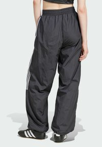 Svarta, löst sittande träningsoveraller i lätt tyg med vita sidostrekar. Elastisk midja och slät yta.