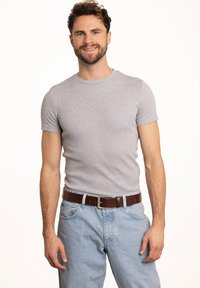 Šedé tričko s krátkým rukávem a ribbed texturou v kombinaci s světle modrými džíny a hnědým koženým pásem. Model stojí před bílým pozadím.