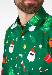 Camicia verde a maniche lunghe con fantasie natalizie, tra cui volti di Babbo Natale, alberi di Natale, ornamenti, stelle e fiocchi di neve.