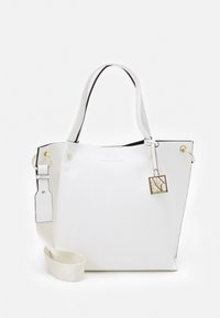 Bílá taška přes rameno s texturovaným povrchem, černými akcenty, zlatými doplňky a odnímatelným popruhem. Obsahuje přívěsek s logem a horní otvory.