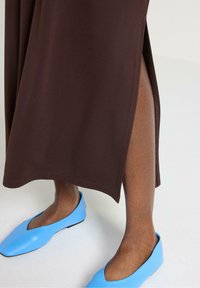 Brun midi kjole med en sideslids, parret med lyseblå fladesko. Glat stoftekstur og en ren, skræddersyet silhuet.