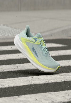 Αθλητικό παπούτσι ανοιχτό μπλε και κίτρινο στον αέρα πάνω από διάβαση πεζών σε άσφαλτο με μικρά θραύσματα γύρω.