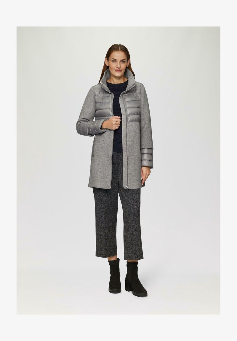 Manteau gris avec devant matelassé et capuche, combiné à une texture lisse semblable à la laine. Assorti à un pantalon gris court et des bottines noires.