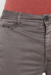 Grå tygbyxor med en slät yta, knappstängning och sidofickor. Midjan är prydd med en kontrasterande rödaktig nyans.