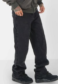 Svarta cargobyxor med lös passform, med flera fickor och fransar i nederkanten. Matchat med svarta sportskor, har tygstrukturen ett slitstarkt utseende.