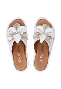 Witte open-teensandalen met een grote metallic gouden en witte bloemenaccent, een gevoerd bruine binnenzool en een gestructureerde witte rubberen zool.