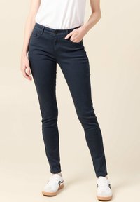 Vaqueros skinny azul oscuro hechos de tejido elástico, con cierre de botón, bolsillos frontales y un acabado elegante. Combinados con zapatillas blancas.