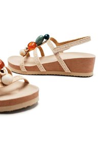 Sandalias de cuña beige con correas trenzadas, decoradas con cuentas coloridas en ámbar, verde y azul. Textura similar al ante en la suela.