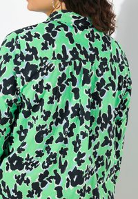 Camicia verde con un motivo astratto nero, colletto classico e dettaglio sulla spalla posteriore. Realizzata in un tessuto leggero.