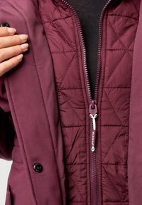 Burgundy insulated jacket with a zippered front, quilted inner lining, pocket detail, and contrasting hardware. Smooth texture, tailored fit.