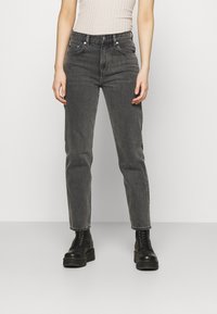 Jeans de tiro alto y pierna recta en denim gris oscuro, con diseño clásico de cinco bolsillos y sutiles detalles de desvanecimiento. Combinados con botas negras de cordones.