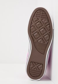 Hnědá gumová podešev tenisky Converse All Star, se strukturovaným vzorem protiskluzu, bílým okrajem a růžovým plátěným bočním panelem.