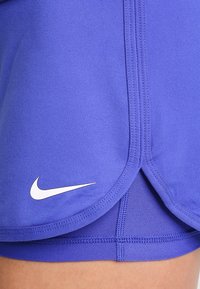 Pantalones cortos deportivos morados con una textura suave, que presentan un logo de Nike blanco y detalles de dobladillo curvados. Tejido elástico para mayor comodidad y movimiento.