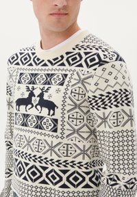 Pull en maille crème avec motifs géométriques bleu marine. Présente un motif de renne, un col rond et des poignets côtelés. Tissu doux et texturé.