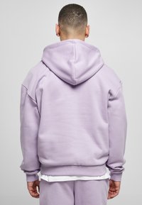 Felpa lilac con taglio rilassato, dotata di un ampio cappuccio e di polsini e orlo a coste. Texture liscia, senza loghi o motivi visibili.