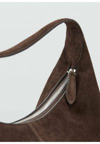 Bolso marrón de ante con forma curvada, equipado con una cremallera plateada y una textura suave. La correa también es de ante, a juego con el color del bolso.