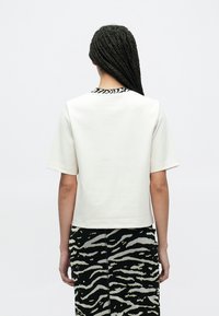 Baltas trumpomis rankovėmis pagamintas viršus iš lygaus audinio, su juodai baltos zebros rašto apykakle ir laisvo silueto. Derinamas su raštuota suknele.