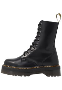 Botas de cuero negro con cordones, puntera redonda, suela de goma gruesa, costuras amarillas y una lengüeta en la parte trasera para facilitar su uso.