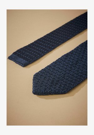 Strikket marineblå slips med tekstureret mønster, der har en spids ende og en lidt bredere base. Blødt stof i en rig blå nuance.