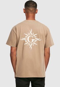 Tan bomulds t-shirt med et hvidt sol design med svulmende former på ryggen. Rund hals, korte ærmer, afslappet pasform. Struktureret finish.