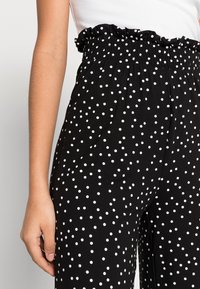 Pantalons noirs à pois blancs, dotés d'une taille élastiquée froncée et d'un tissu doux. Le design comprend une coupe décontractée et des jambes larges.