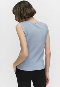 Vaaleansinen, ribatty ilmanhiha-toppi, jossa on pyöreä kaula-aukko ja pieni nappi takana, yhdistettynä mustiin housuihin.