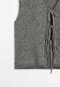 Gray knitted vest featuring a V-neckline, front tie closure, and a loose fit. Textured fabric with a blend of light and dark threads.
