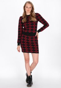Musta ja punainen argyle-kuvioitu mekko pitkilla hihoilla ja kapealla siluetilla. Neulottu materiaali, jossa on ribbauskäreet ja helma. Mustat nauhakenkäbootsit.