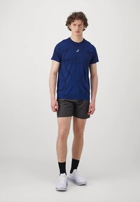 Granatowy t-shirt z krótkim rękawem i okrągłym dekoltem; zestawiony z czarnymi szortami i białymi tenisówkami. Prosty, sportowy design z akcentem w postaci logo.