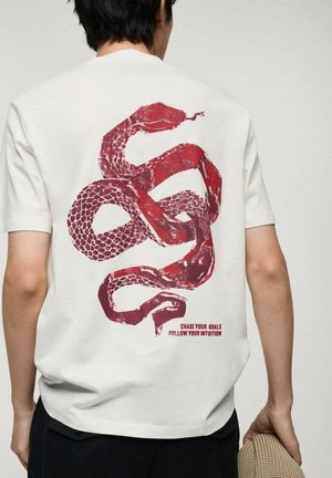 T-shirt en coton blanc avec un imprimé serpent rouge dans le dos, accompagné du texte « POURSUIVEZ VOS OBJECTIFS SUIVEZ VOTRE INTUITION ». Manches courtes.