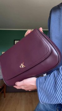 Dark burgundy leather handbag with a smooth texture, gold hardware, and stitched detailing. Features a logo and a chain strap.