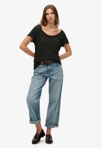 Camiseta negra de manga corta y escote en pico combinada con unos vaqueros de cintura alta, de color azul claro y con dobladillo, y unos mocasines oscuros con suelas texturizadas.