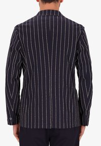 Blazer blu navy con strisce verticali bianche e beige. Presenta un colletto a punta e polsini con bottoni. Realizzato in tessuto testurizzato.