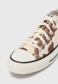 Pantof sport din material textil cu model piele de vacă în nuanțe de bej și crem. Are vârf de cauciuc alb, garnitură neagră și șireturi bej.