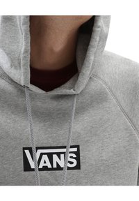 Sudadera con capucha gris con cordón, que presenta un logo de Vans negro en el frente. La tela es suave; la textura parece lisa con un ajuste ceñido.