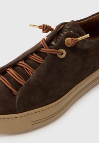 Brown suede sneaker with brown elastic laces and gold-tone eyelets. Features a textured rubber sole with a smooth finish.