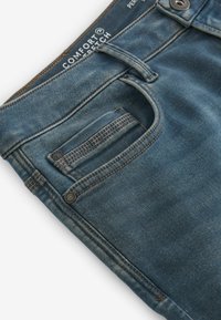 Plave traperice s ravnim krojem, s ušivenim džepom, mesinganom tipkom i oznakom "Comfort Stretch" na pojasu.