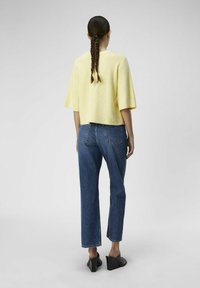 Top giallo a righe con maniche corte abbinato a jeans in denim blu a vita alta. I jeans hanno una vestibilità dritta e tasche posteriori. Mule neri con tacco.