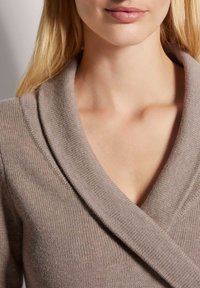 Beige Strickpullover mit einem breiten, umgeschlagenen Kragen, der eine glatte Textur und einen tiefen V-Ausschnitt zeigt. Nahaufnahme des Ausschnittbereichs.