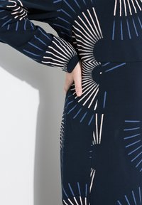 Marindräkt med ett geometriskt mönster av radiella linjer i mjuk rosa och ljusare blå. Tillverkad av strukturerat tyg med en avslappnad passform och manschetter.