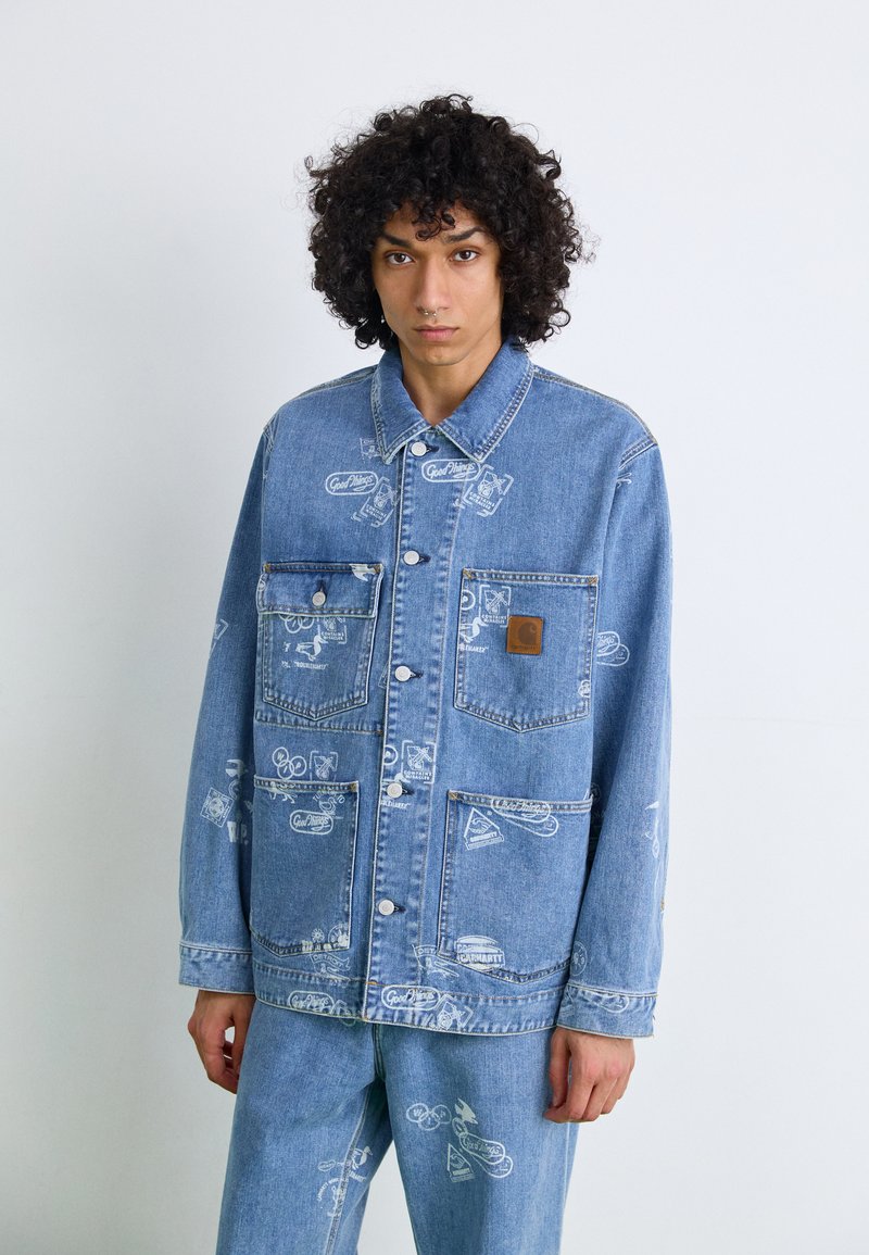 Light blue denim jacket with large chest pockets, button closure, and repeated white graphic prints. Features a logo patch on the left pocket.