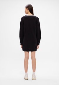 Μαύρο φόρεμα φούτερ με μακριά μανίκια, ριμπ κολάρο με δύο λευκές ρίγες και χαλαρή εφαρμογή, φτάνοντας στο μέσο του μηρού.