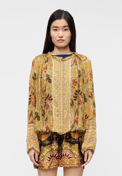 Blouse jaune à motifs avec manches longues, encolure froncée et couture décorative. Associée à un short multicolore avec un design audacieux.