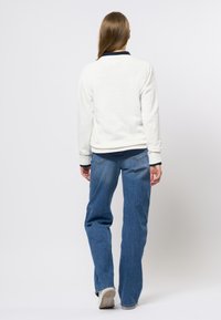 Hvit sweatshirt med marineblå krage, lange ermer og ribbede mansjetter, kombinert med blå rette jeans og hvite joggesko. Rent design.