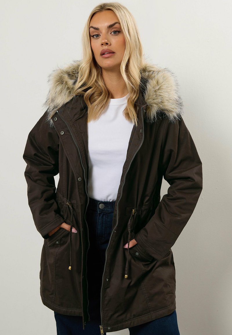 Brun parka-jacka med pälsfållad huva, dragsko i midjan, zipförslutning och sidofickor. Mjuk tyg med en något glansig textur.