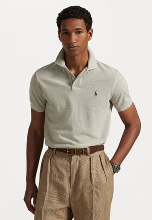 Vaaleanharmaa polo-paita, jossa on teksturoitu kudos ja pieni vihreä logo rinnassa, yhdistettynä ruskeisiin ruudullisiin housuihin ja niihin sopivaan vyöhön.