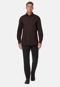 Brązowa koszula z długim rękawem, z wyraźnym kołnierzykiem i subtelną fakturą, w połączeniu z ciemnymi spodniami i brązowymi butami.